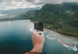 man holding a GoPro travel camera over the coastline of an island