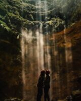 Two girls in Jomblang cave standing looking at the sunbeams coming through the top of the verticle cave