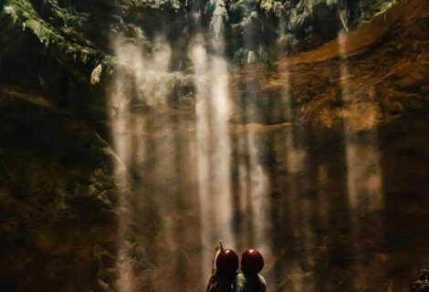 Two girls in Jomblang cave standing looking at the sunbeams coming through the top of the verticle cave