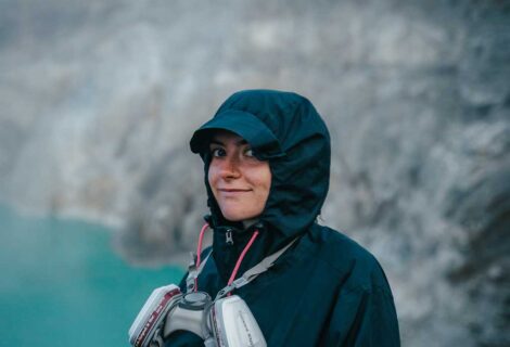 Kizzi standing at the top of Mount Ijen with the blue lake in the background wearing a gas mask around her neck